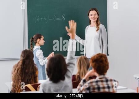 professeur souriant regardant un élève levant la main sur un premier plan flou Banque D'Images