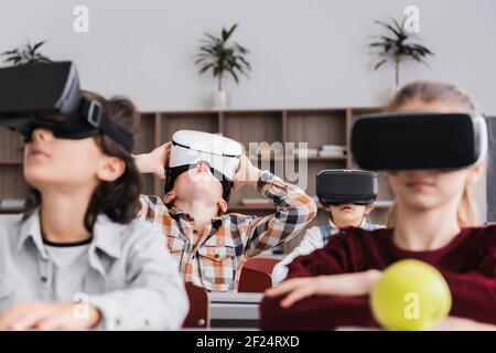 mise au point sélective d'un élève étonné dans un casque vr près des camarades de classe sur un arrière-plan flou Banque D'Images