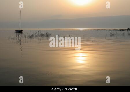 Lever du soleil sur le lac. Bateau flottant sur l'eau calme sous un coucher de soleil étonnant. Banque D'Images