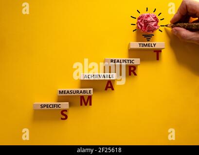 Symbole professionnel et INTELLIGENT. Main d'homme d'affaires. Blocs en bois avec des mots 'SMART, spécifique mesurable réaliste réalisable en temps opportun'. Fond jaune, cop Banque D'Images