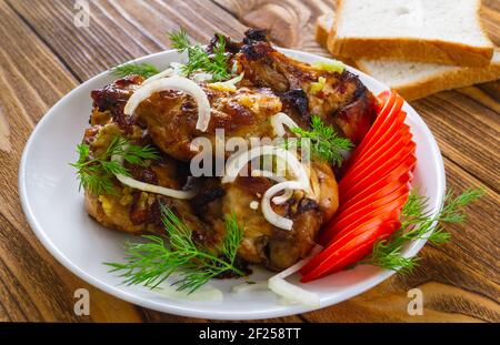 Gros plan sur les ailes de poulet frites, avec des tomates fraîches, des oignons, de l'aneth, de l'ail et du pain sur fond de bois. Le concept de nourriture de viande. Banque D'Images