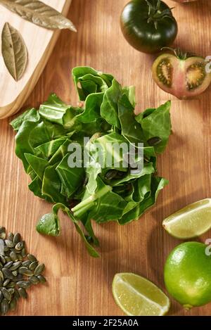 Feuilles d'épinards sur une table de cuisine en bois. Il y a une planche à découper avec des feuilles de Laurier, des tomates, de la chaux et des graines. Keto Diet pour une alimentation saine. Légumes frais Banque D'Images