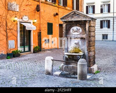 La fontaine de rione Borgo est protégée par deux petites colonnes reliées par une barre de fer, se compose d'un simple aedicule rectangulaire de travertin, pignon en haut et appuyé contre une construction en brique. La voûte supérieure a un blason papal - Rome, Italie Banque D'Images