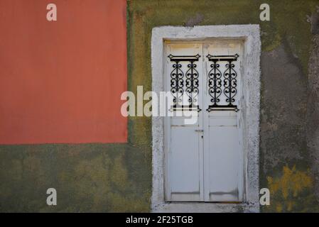 Façade traditionnelle de maison ancienne avec une porte d'entrée blanche faite sur mesure et des grilles en fer artisanales sur un mur abîmé à Lavrion, Attica Grèce. Banque D'Images