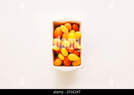 Bol en céramique rectangulaire et rond avec tomates cerises orange, jaune et rouge sur fond blanc et espace de copie Banque D'Images