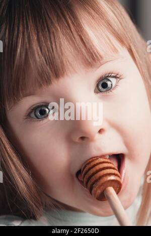 Gros plan portrait de drôle belle petite fille manger du miel. Photo de haute qualité Banque D'Images