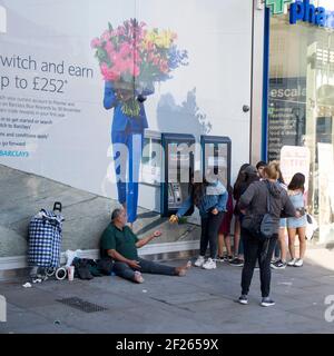 Londres, Royaume-Uni - 20 septembre 2020, UNE jeune fille donne des almes à un mendiant roumain assis près du cashpoint de Barclay Banque D'Images