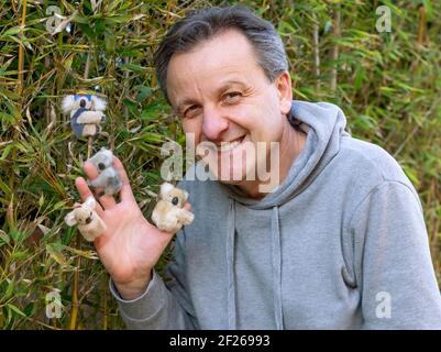 Un homme d'âge moyen joue avec de petits animaux en peluche en forme de koala Banque D'Images