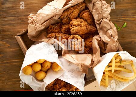 Nuggets, boules de pommes de terre, frites et ailes dans une boîte en papier sur fond de bois. Photo de haute qualité Banque D'Images