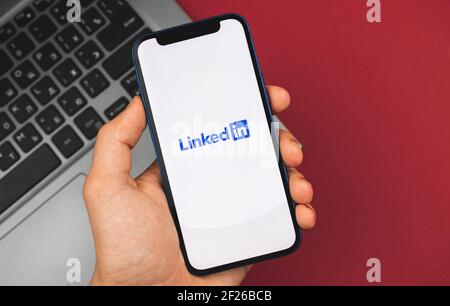 Kharkov, Ukraine - 9 mars 2021 : l'homme tient un smartphone avec une application LinkedIn ouverte, une photo de fond d'entreprise Banque D'Images