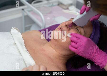 Dispositif de cavitation. L'esthéticienne guide doucement l'échographe sur le visage du client pour exfolier l'épiderme. Banque D'Images