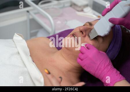 Dispositif de cavitation. L'esthéticienne guide doucement l'échographe sur le visage du client pour exfolier l'épiderme. Banque D'Images