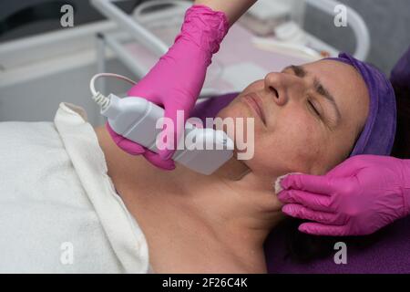 Dispositif de cavitation. L'esthéticienne guide doucement l'échographe sur le visage du client pour exfolier l'épiderme. Banque D'Images