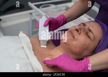 Dispositif de cavitation. L'esthéticienne guide doucement l'échographe sur le visage du client pour exfolier l'épiderme. Banque D'Images