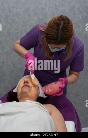 Un masque professionnel aux algues est appliqué sur le visage du client avec une spatule Banque D'Images