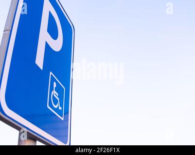 Panneau de stationnement bleu à angle bas pour handicapés avec gros plan ciel transparent Banque D'Images