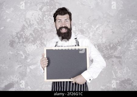 publicité de votre produit. hipster cook ou barista présentant le produit. sentez le succès. menu du café. cuisine ravie. cuisine du chef de restaurant. barbu brutal avec tableau noir. Banque D'Images