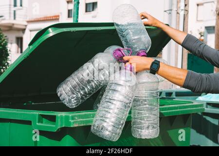 L'homme jette de grandes bouteilles d'eau en plastique vides vers le conteneur d'ordures principal Banque D'Images
