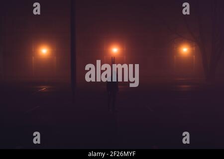 Homme méconnaissable au milieu d'une autoroute avec des lumières rouges la nuit Banque D'Images