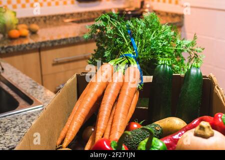 Détail d'une boîte pleine de fruits et légumes biologiques sur un comptoir de cuisine Banque D'Images