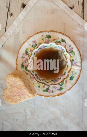 Tasse de thé d'en haut. Gros plan. Tasse à thé et soucoupe vintage avec teabag steeping et scone en forme de cœur. Sur lin irlandais blanc vintage. Banque D'Images