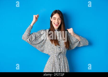 Une jeune fille souriante et excitée montrant la langue et dansant avec les mains levées, célébrant la victoire ou la réussite, gagnant le prix, se tenant à la hauteur Banque D'Images