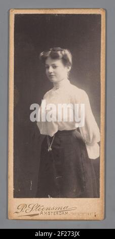 Portret van een jonge vrouw.jeune femme debout, dans un chemisier clair et une jupe sombre, avec les mains sur le dos, sur un fond sombre. Banque D'Images