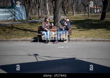 Belgrade, Serbie, 7 mars 2021 : deux femmes assises sur un banc, prenant du café et du soleil Banque D'Images