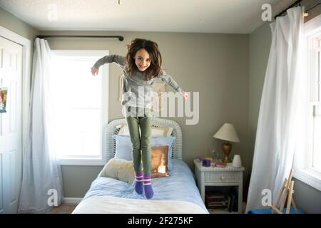 Petite fille sautant sur le lit dans la chambre ensoleillée. Banque D'Images