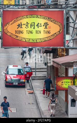 Île de Hong Kong, Chine - 14 mai 2010 : rue commerçante avec taxi rouge montre panneau d'affichage de la boutique de médecine chinoise Beijing Tong Ren Tang, dans le centre de Mid-le Banque D'Images