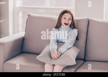 Portrait d'une jolie petite fille insouciante et gaie assise sur un divan repos s'amuser à la maison plat à l'intérieur Banque D'Images