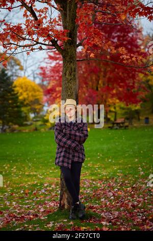 Jeune femme posant à côté d'un arbre pendant l'automne. Entouré de feuilles de couleur automnale dans Stewart Park. Banque D'Images