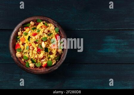 Couscous végétalien avec des légumes, des amandes, des pois chiches et des herbes, tiré d'en haut sur un fond en bois sombre Banque D'Images