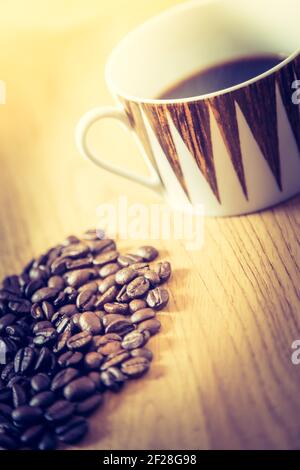 Gros plan sur les grains de café fraîchement torréfiés et la tasse à café sur fond en bois Banque D'Images