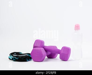 Gants de sport, paire d'haltères violettes et bouteille d'eau sur fond blanc Banque D'Images