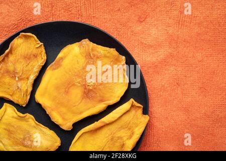tranches de mangue séchée sur une assiette noire contre papier à écorce texturée avec espace de copie Banque D'Images