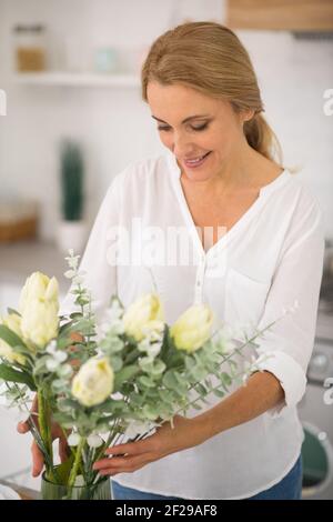 Jolie femme de ménage mettant des fleurs dans le vase Banque D'Images