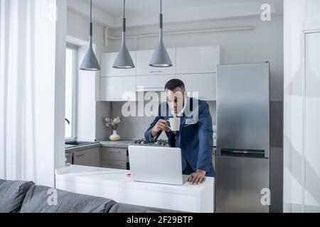 Élégant homme à la peau sombre qui lit quelque chose sur un ordinateur portable et qui a l'air excité Banque D'Images