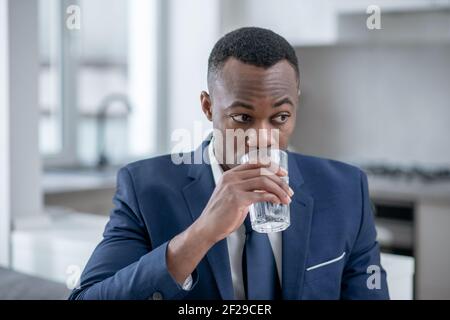 Élégant homme à la peau sombre qui a l'air inquiet et qui a l'eau potable Banque D'Images