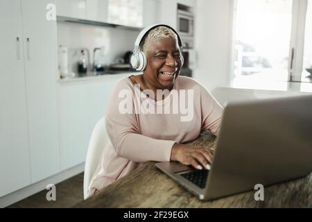 Femme âgée utilisant un ordinateur portable tout en portant un casque à la maison - Concept de mode de vie et de technologie joyeux pour les personnes âgées - concentrez-vous sur le visage Banque D'Images
