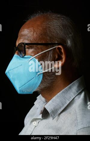 Portrait d'un Indien de 60 ans portant un masque bleu, isolé sur un fond noir, afin de se protéger de la COVID-19. Banque D'Images