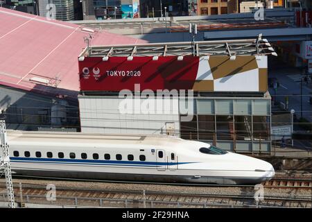 Un train à grande vitesse qui passe devant la place des sports de Tokyo, orné des logos olympiques et paralympiques de 2020. La voie express de Shoto est en arrière-plan. Banque D'Images