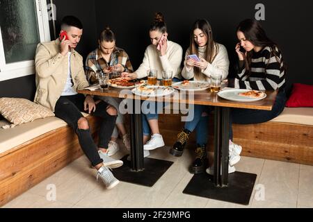 un groupe de jeunes utilisent leur téléphone portable dans une pizzeria Banque D'Images