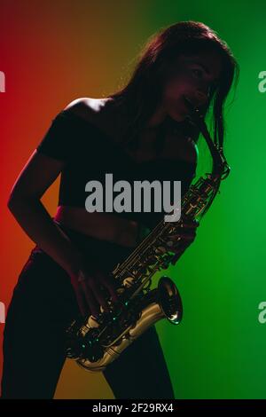 Silhouette de jeune fille avec saxophone posé isolé sur fond vert-rouge. Banque D'Images