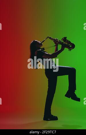 Portrait d'une jeune fille avec saxophone posé isolé sur fond vert-rouge. Banque D'Images