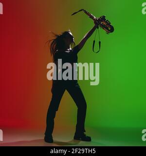 Portrait d'une jeune fille avec saxophone posé isolé sur fond vert-rouge. Banque D'Images