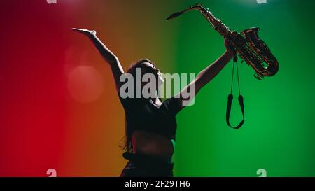 Portrait d'une jeune fille avec saxophone posé isolé sur fond vert-rouge. Banque D'Images