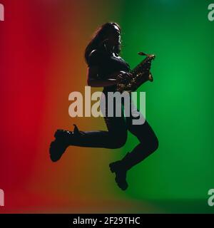 Silhouette de jeune fille avec saxophone posé isolé sur fond vert-rouge. Banque D'Images