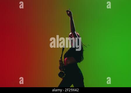 Portrait d'une jeune fille avec saxophone posé isolé sur fond vert-rouge. Banque D'Images