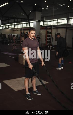 Plan vertical d'un homme athlétique musclé après s'être posé faites de l'exercice avec des cordes de combat à la salle de sport cross fit Banque D'Images